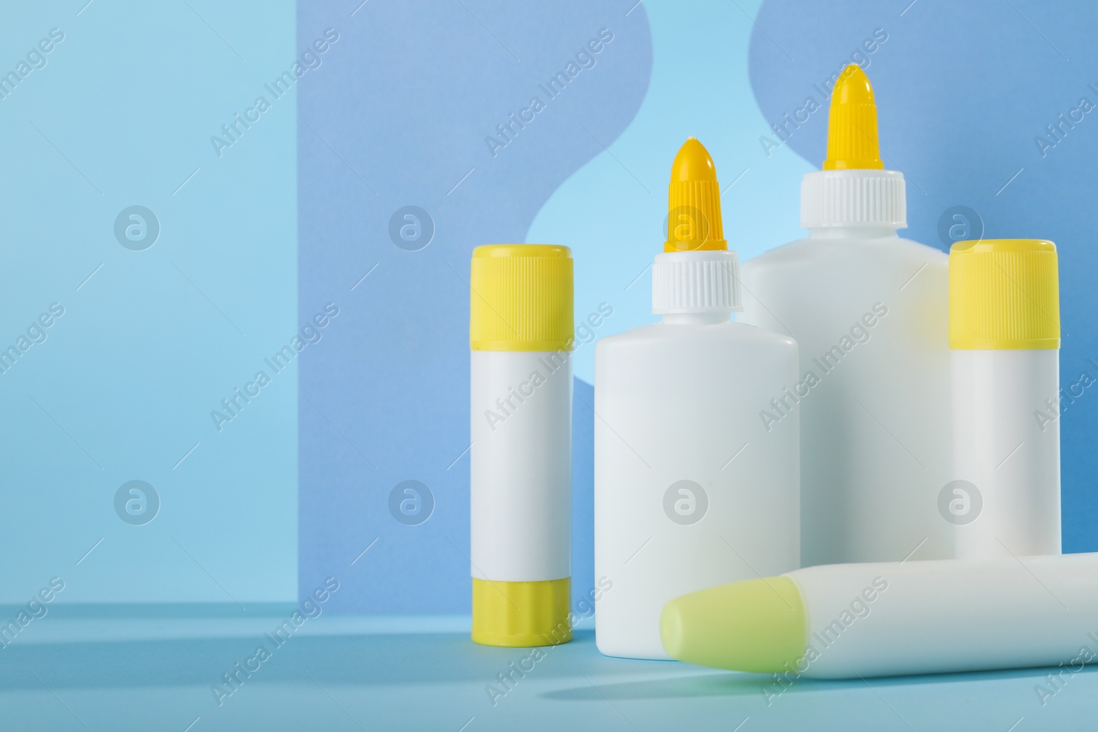 Photo of Different types of glue and paper cutouts on light blue background, space for text