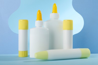 Photo of Different types of glue and paper cutouts on light blue background