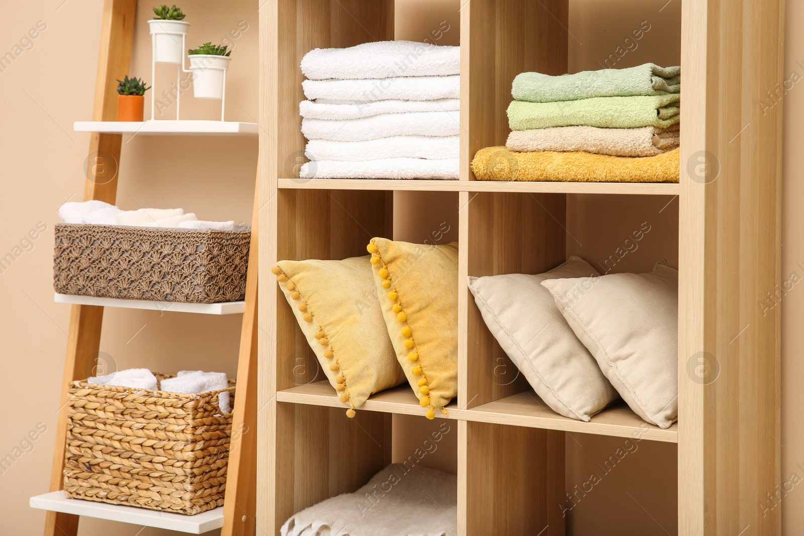 Photo of Folded towels and pillows on shelving unit indoors. Home textile storage