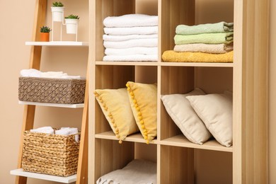 Photo of Folded towels and pillows on shelving unit indoors. Home textile storage