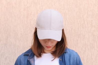 Photo of Woman in stylish baseball cap near beige wall. Mockup for design