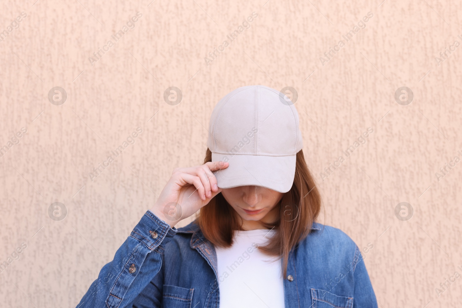 Photo of Woman in stylish baseball cap near beige wall. Mockup for design