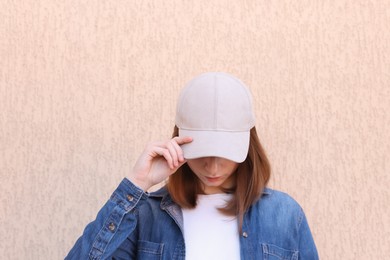 Photo of Woman in stylish baseball cap near beige wall. Mockup for design