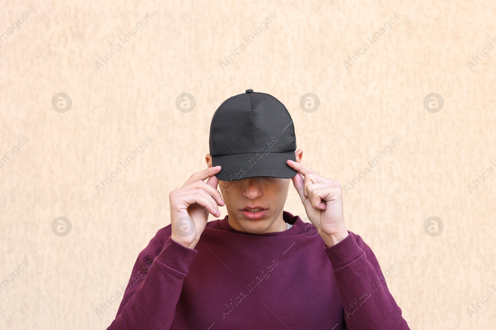 Photo of Man in stylish baseball cap near beige wall. Mockup for design