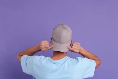 Photo of Man in stylish baseball cap on violet background, back view. Mockup for design