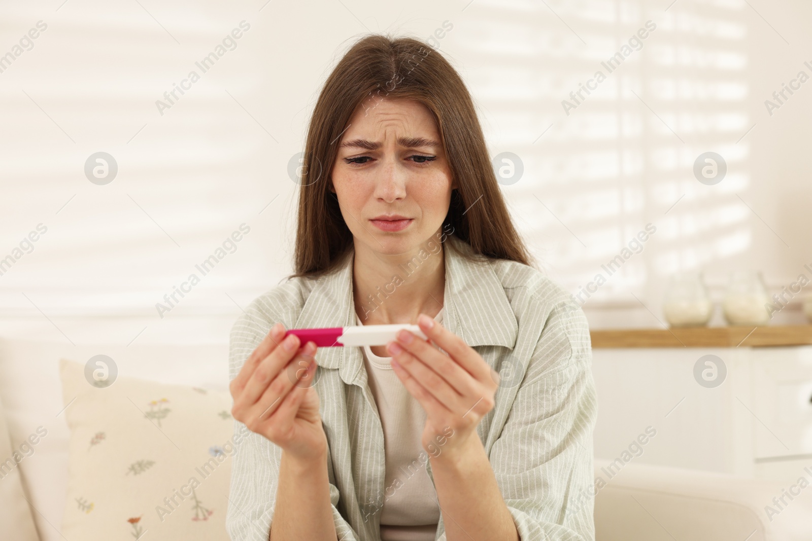 Photo of Upset woman with negative pregnancy test at home