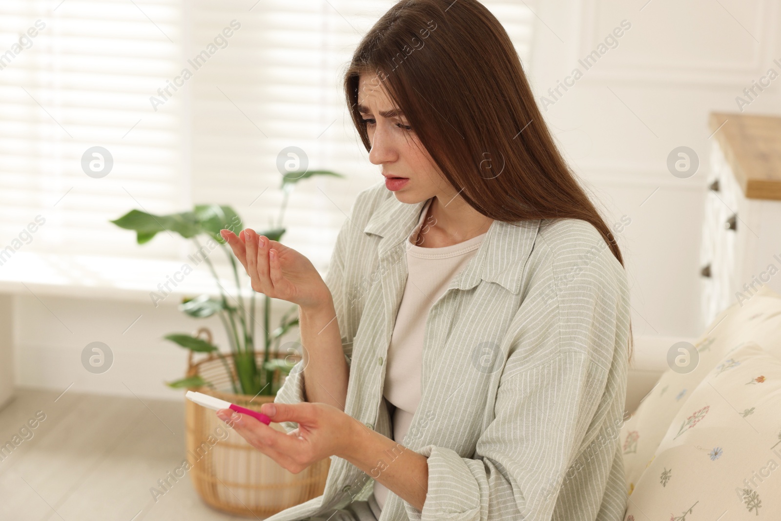 Photo of Upset woman with negative pregnancy test on sofa at home