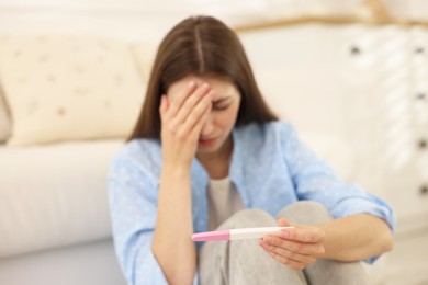 Photo of Upset woman with negative pregnancy test at home, selective focus