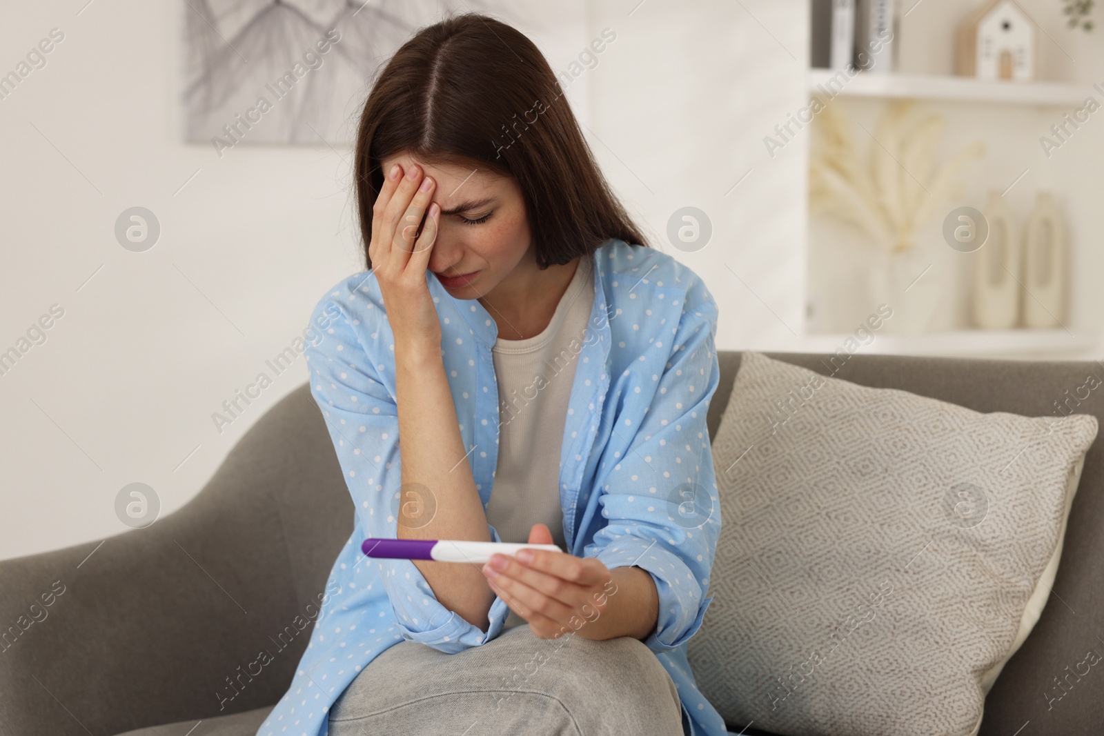 Photo of Upset woman with negative pregnancy test on sofa at home