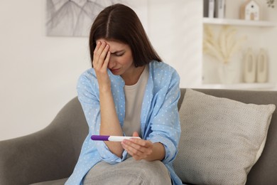 Photo of Upset woman with negative pregnancy test on sofa at home