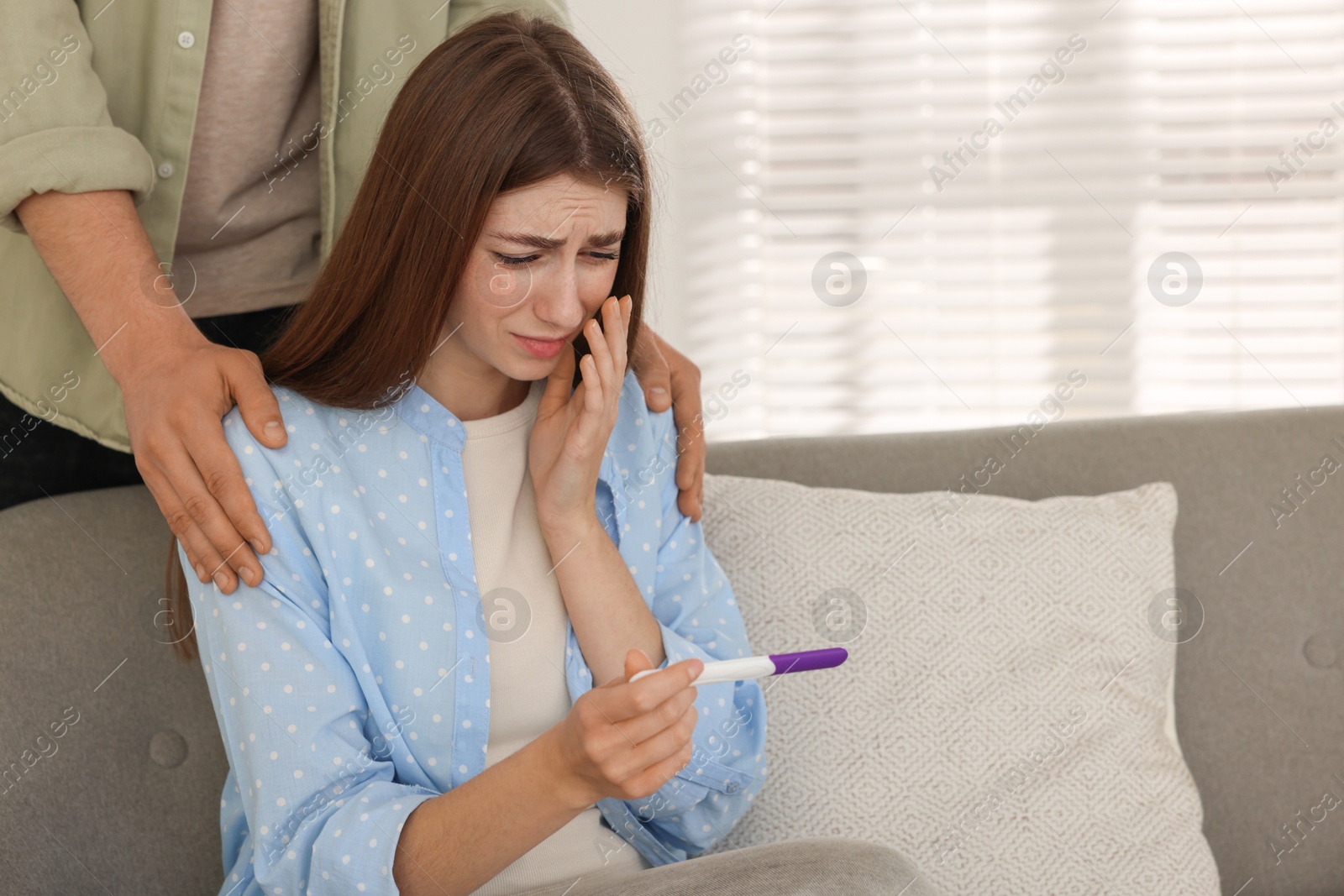 Photo of Upset woman with negative pregnancy test indoors. Man supporting his wife at home