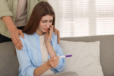 Photo of Upset woman with negative pregnancy test indoors. Man supporting his wife at home