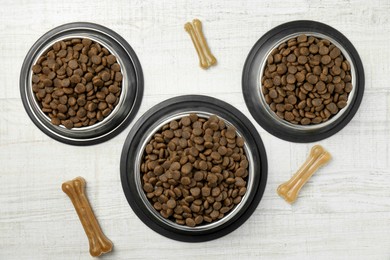 Photo of Dry pet food in feeding bowls and chew bones on floor, flat lay