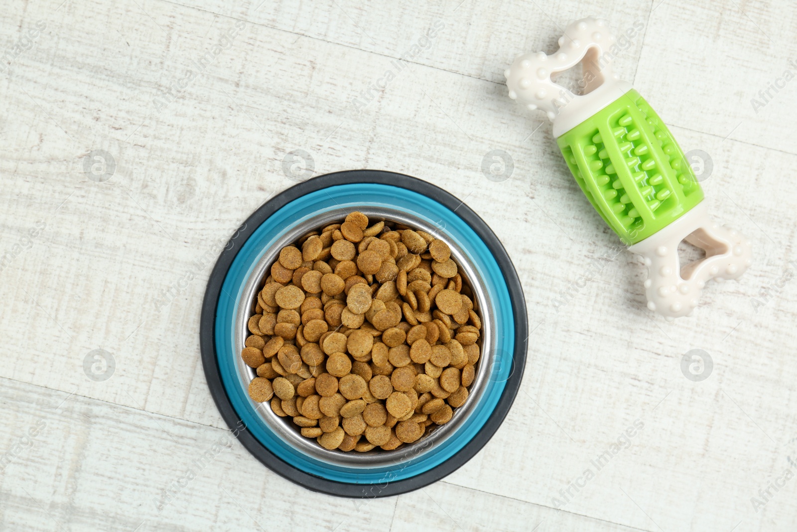 Photo of Dry pet food in feeding bowl and chew bone on floor, top view