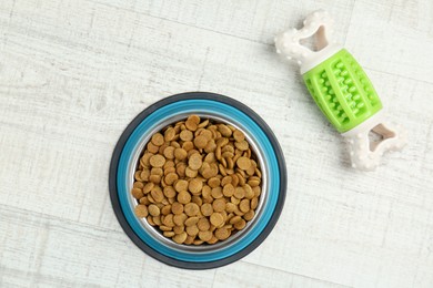 Photo of Dry pet food in feeding bowl and chew bone on floor, top view