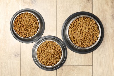 Photo of Dry pet food in feeding bowls on wooden floor, flat lay