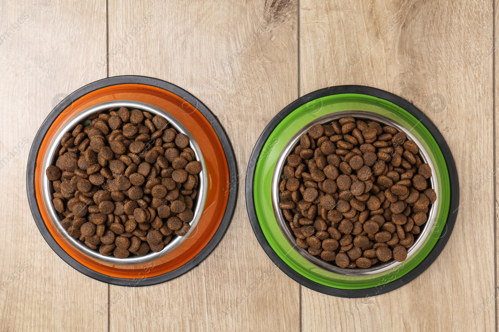 Photo of Dry pet food in feeding bowls on wooden floor, top view