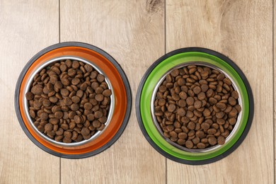 Photo of Dry pet food in feeding bowls on wooden floor, top view