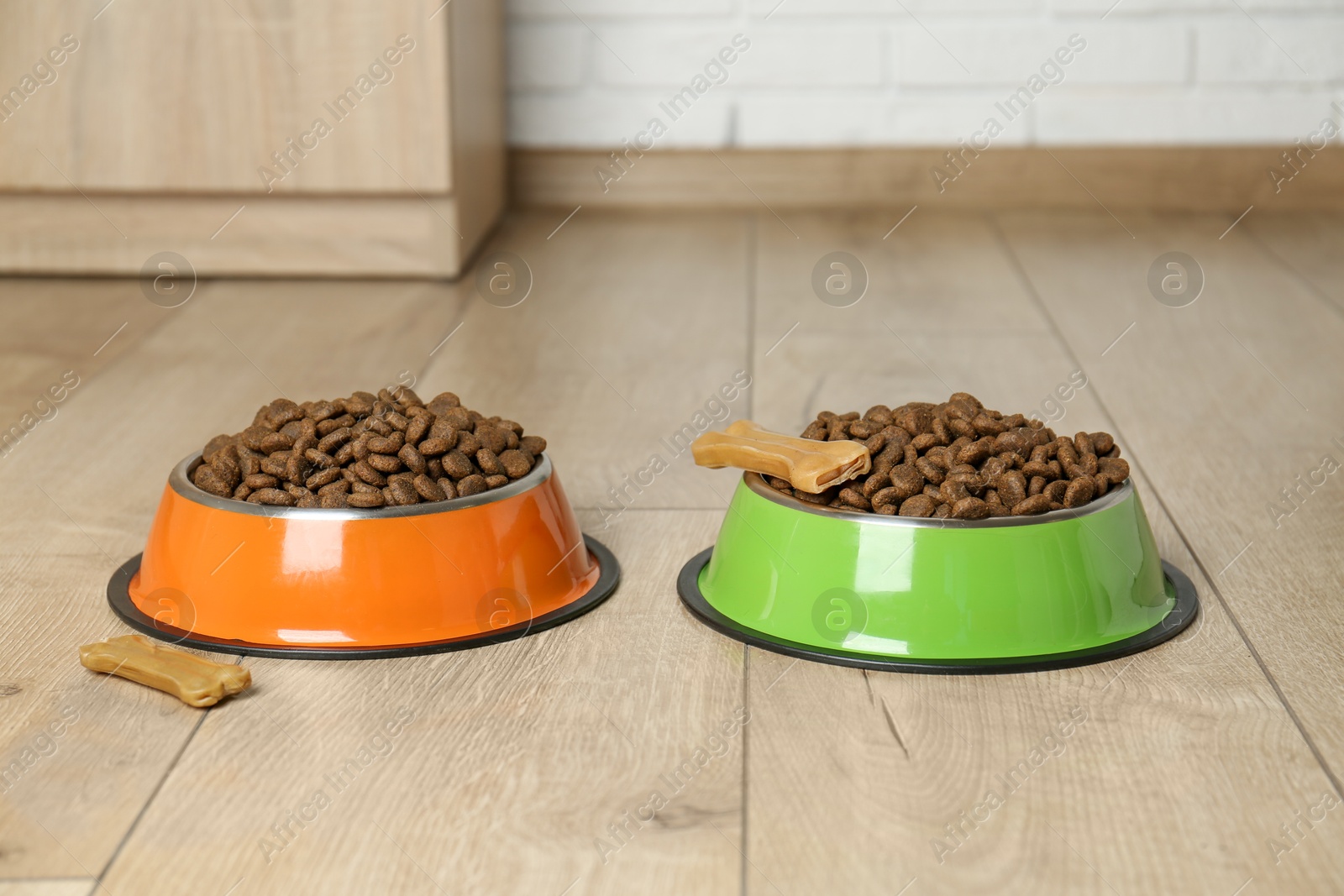 Photo of Dry pet food in feeding bowls and chew bones on floor indoors