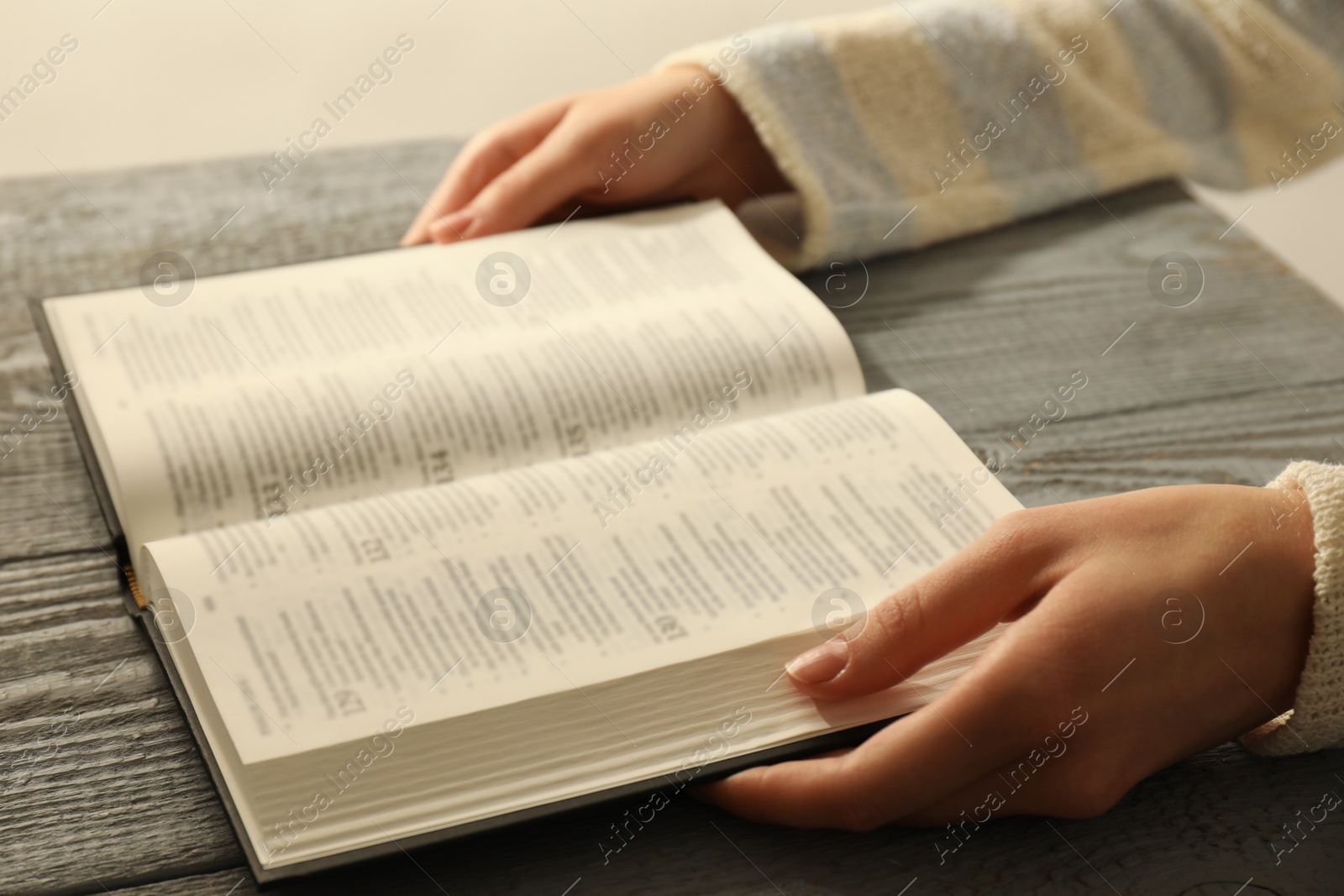 Photo of Woman with open Holy Bible in English language at wooden table, closeup