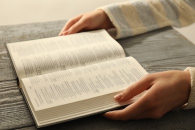 Photo of Woman with open Holy Bible in English language at wooden table, closeup