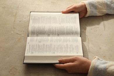 Photo of Woman reading Holy Bible in English language at beige table, closeup