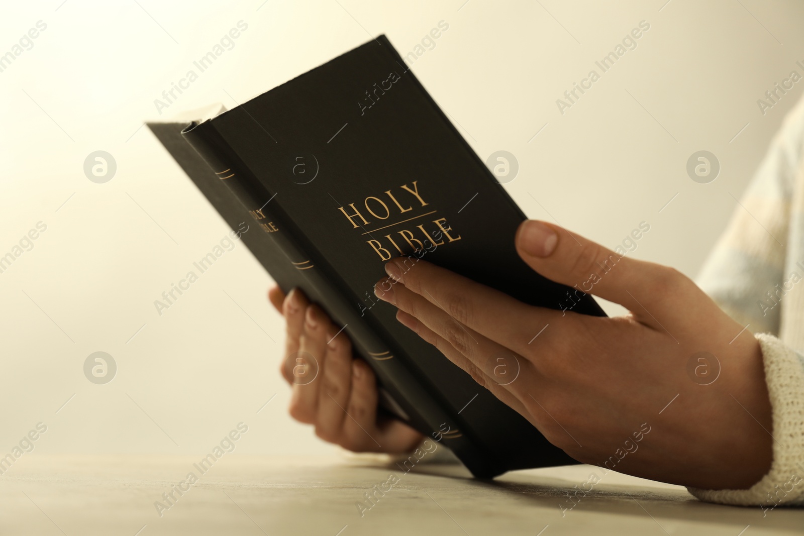 Photo of Woman reading Holy Bible at beige table, closeup