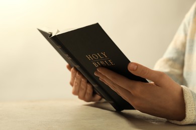 Photo of Woman reading Holy Bible at beige table, closeup