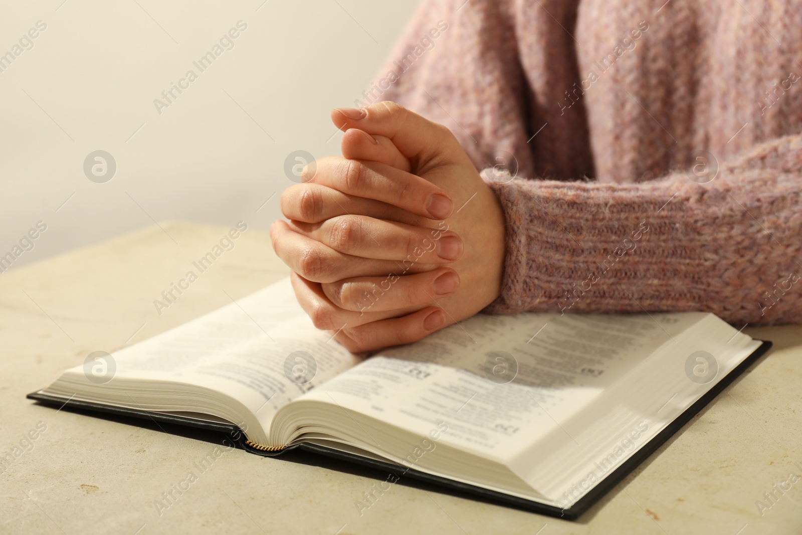 Photo of Woman with open Holy Bible in English language praying at beige table, closeup