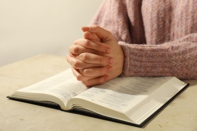 Photo of Woman with open Holy Bible in English language praying at beige table, closeup