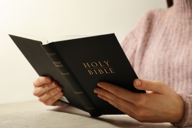 Photo of Woman reading Holy Bible at beige table, closeup