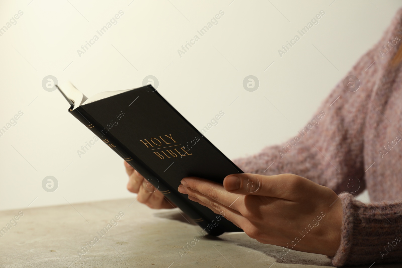 Photo of Woman reading Holy Bible at beige table, closeup