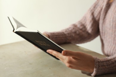 Photo of Woman reading Holy Bible at beige table, closeup