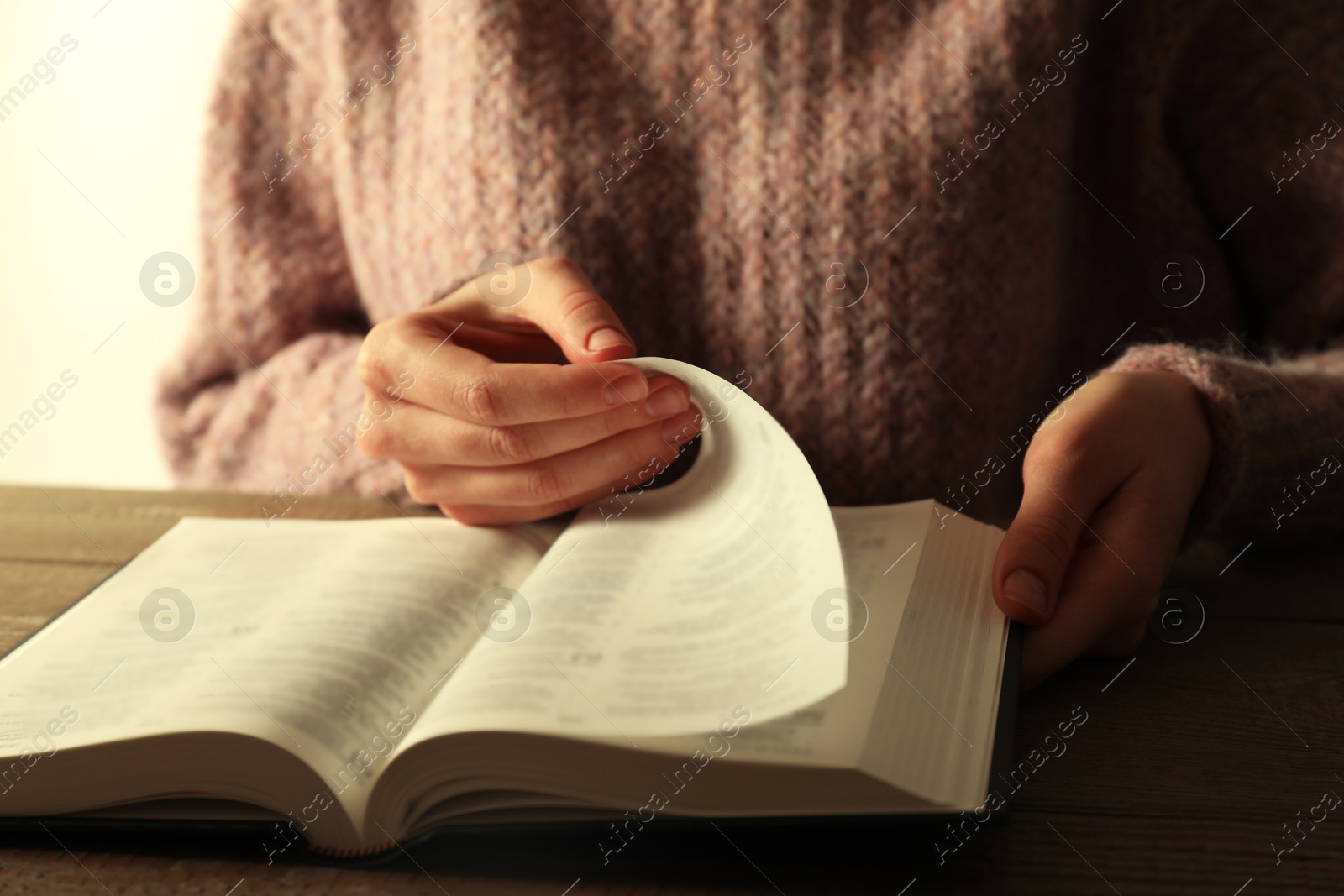 Photo of Woman reading Holy Bible in English language at wooden table, closeup