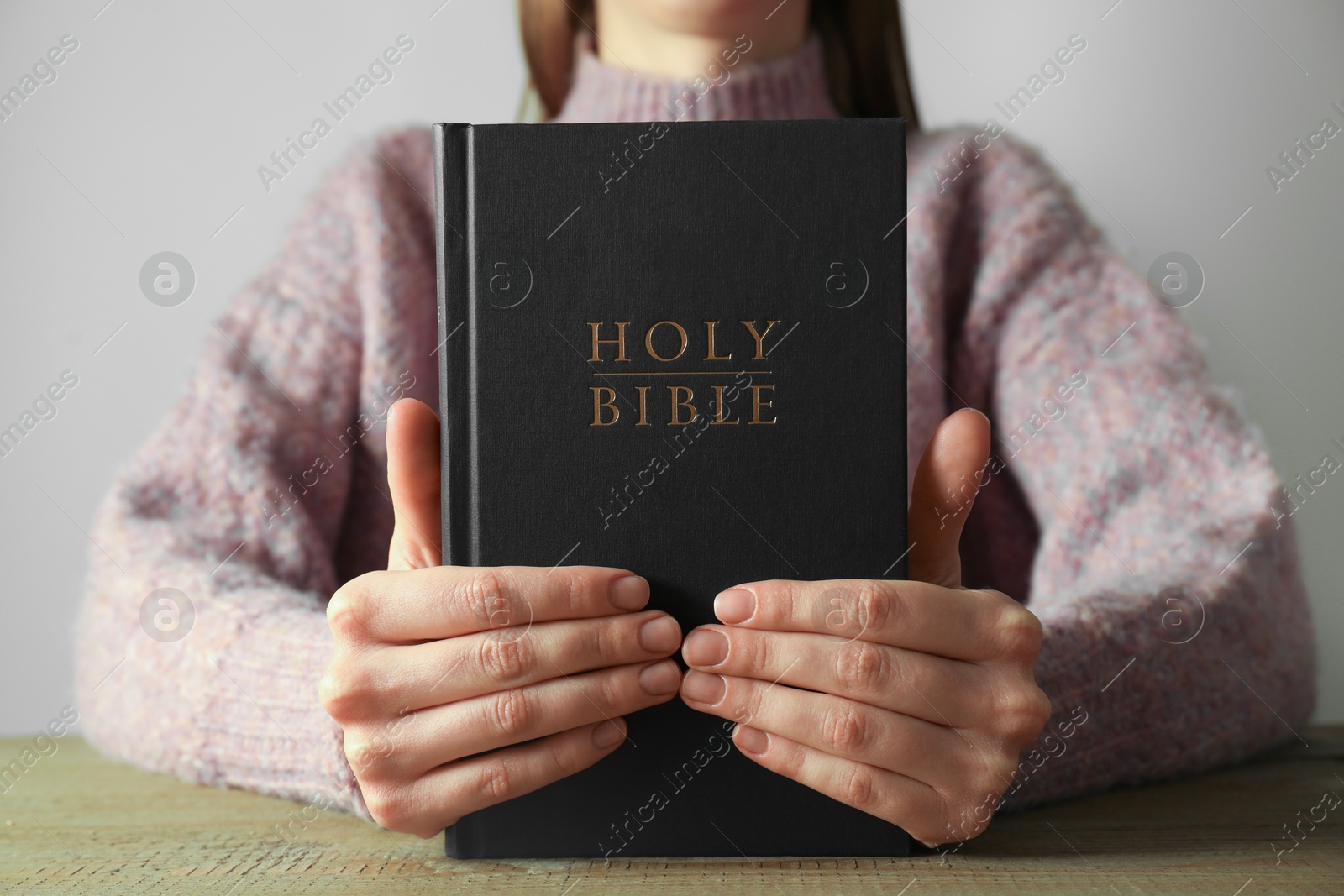 Photo of Woman with hardcover Holy Bible at wooden table, closeup