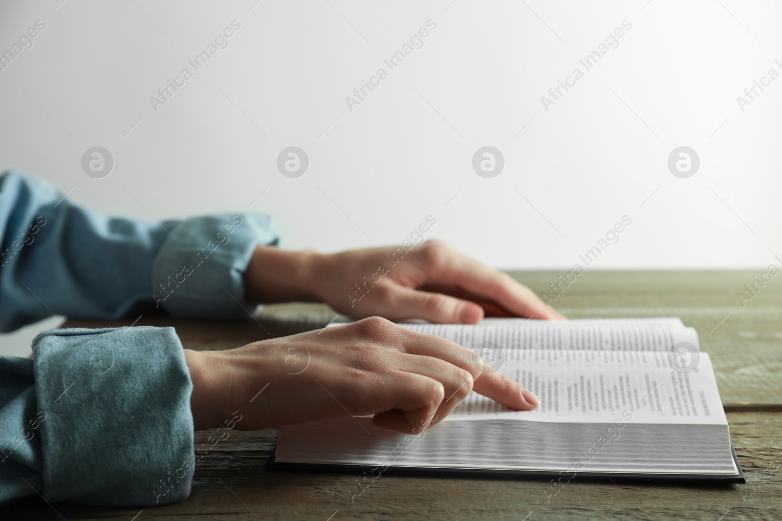 Photo of Woman reading Holy Bible at wooden table, closeup