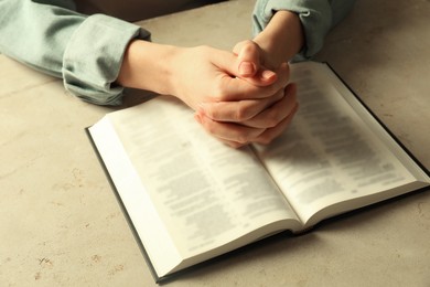 Photo of Woman with open Holy Bible in English language praying at beige table, closeup