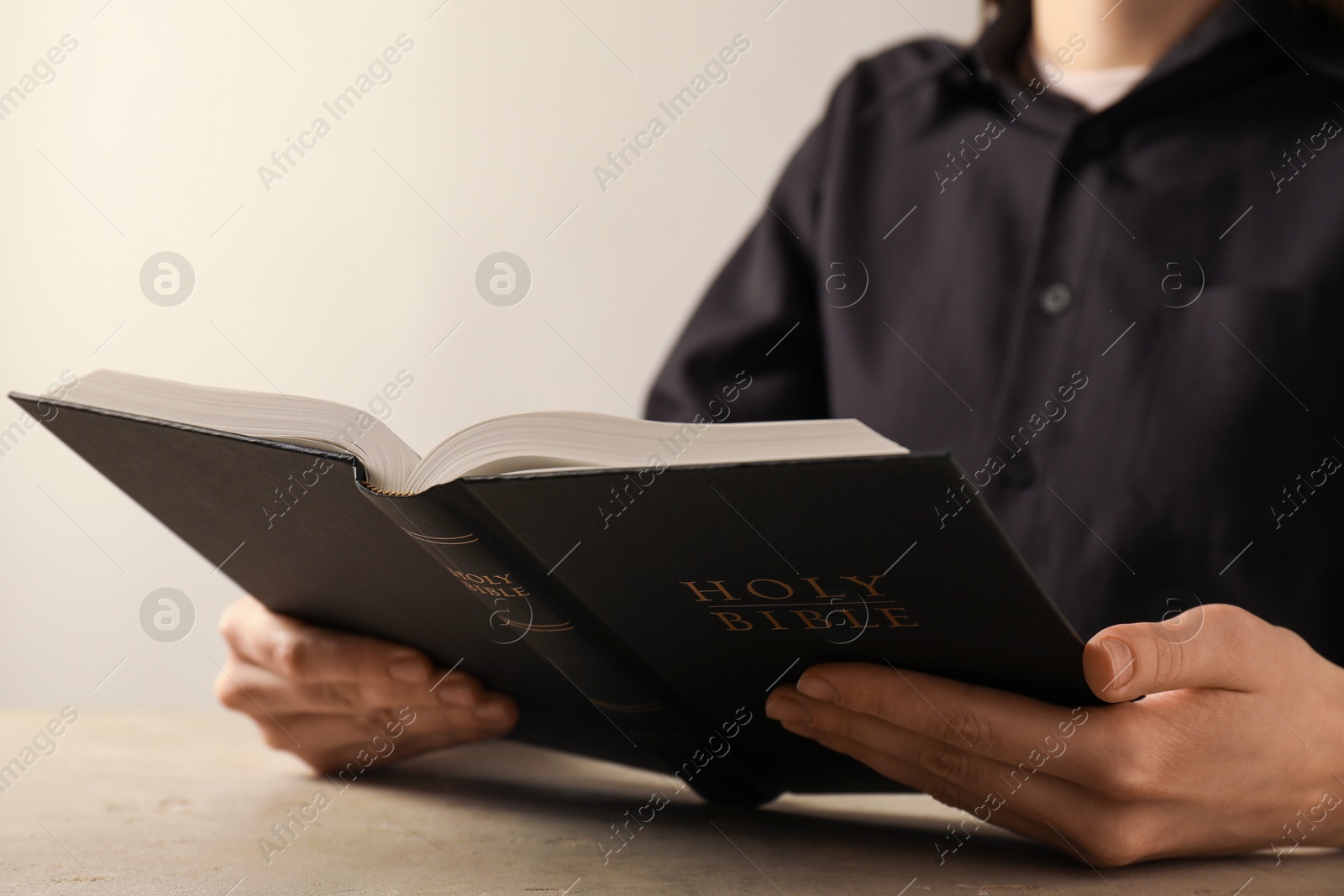 Photo of Woman reading Holy Bible at beige table, closeup