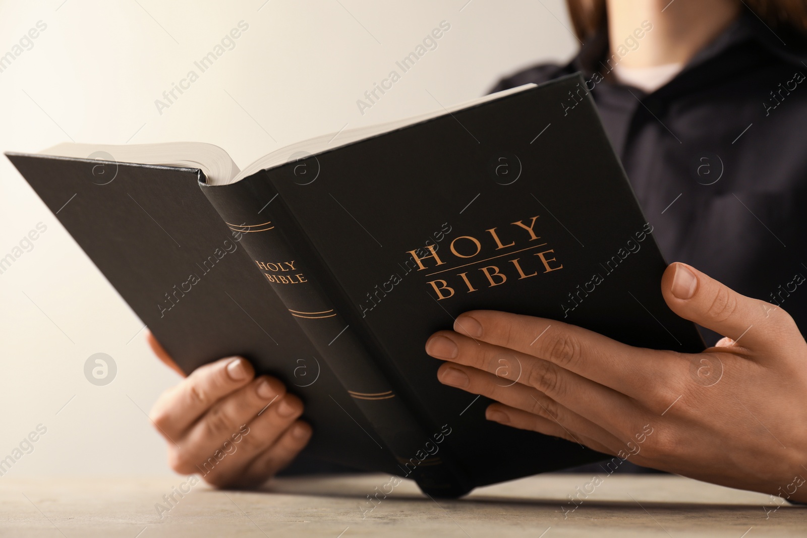 Photo of Woman reading Holy Bible at beige table, closeup