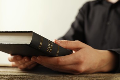 Photo of Woman with hardcover Holy Bible at wooden table, closeup