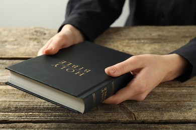 Photo of Woman with hardcover Holy Bible at wooden table, closeup