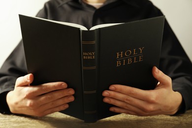 Photo of Woman reading Holy Bible at wooden table, closeup