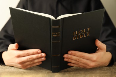 Photo of Woman reading Holy Bible at wooden table, closeup