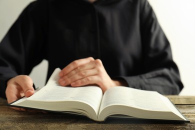 Photo of Woman reading Holy Bible at wooden table, closeup