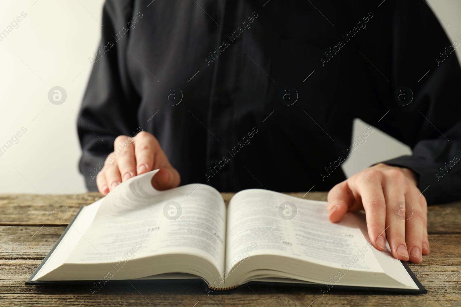 Photo of Woman reading Holy Bible in English language at wooden table, closeup