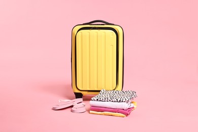 Photo of Suitcase, flip-flops and folded clothes on pink background