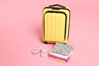 Photo of Suitcase, flip-flops and folded clothes on pink background