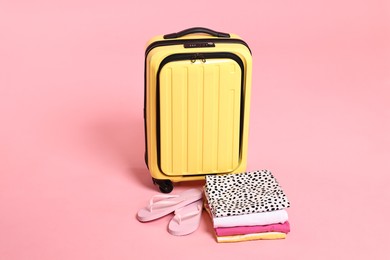 Photo of Suitcase, flip-flops and folded clothes on pink background