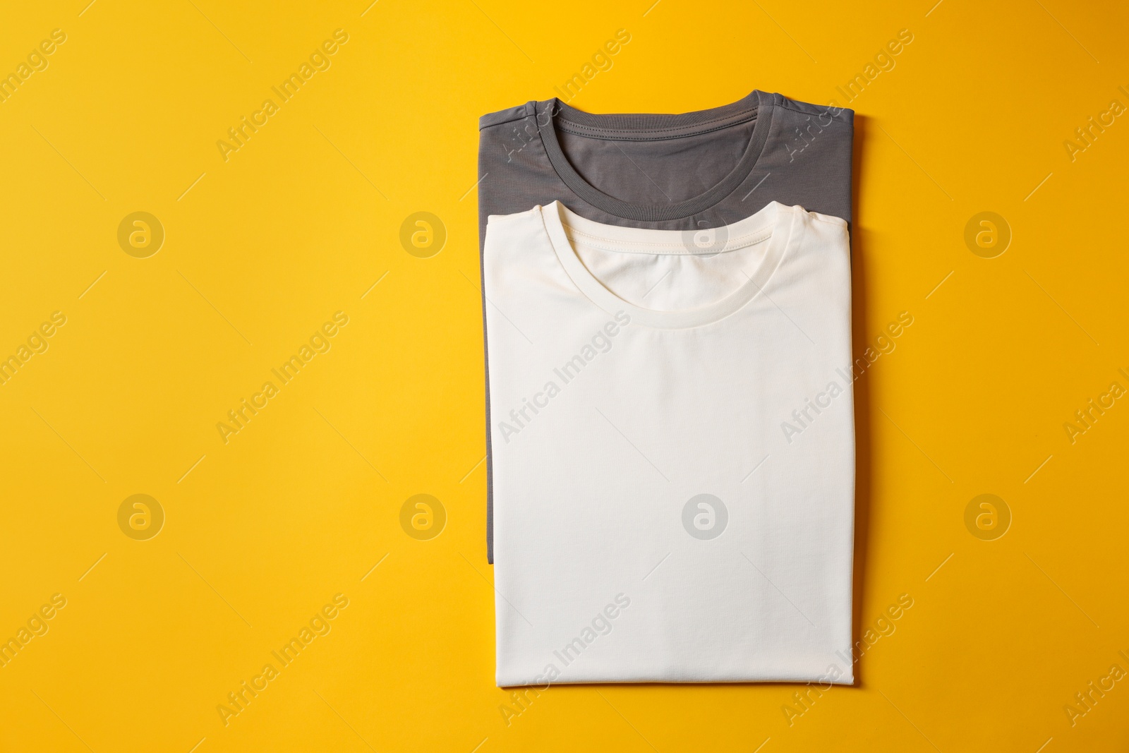 Photo of Different blank t-shirts on yellow background, top view. Mockup for design