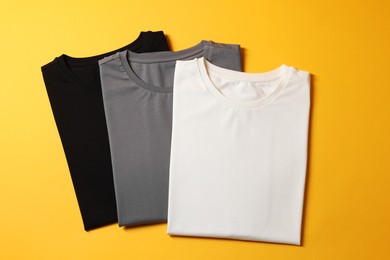 Photo of Different blank t-shirts on yellow background, top view. Mockup for design